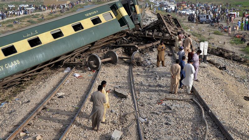 Local residents examine damaged cars of a passenger train which was derailed near Nawabshah,...