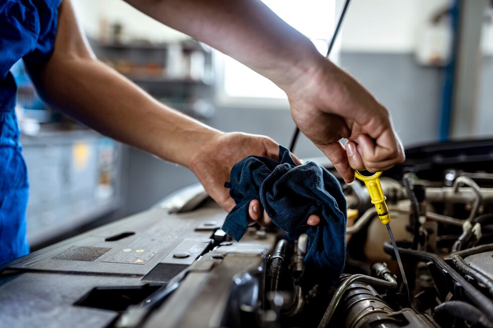 Photo of male mechanic measuring the oil level of an engine at an auto shop. Mechanic checking...