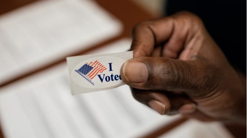 A poll worker in Richmond holds an "I Voted" sticker.